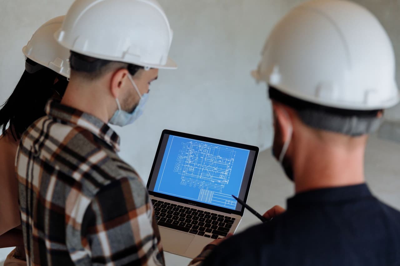 Two people in hard hats reviewing building plans on a laptop